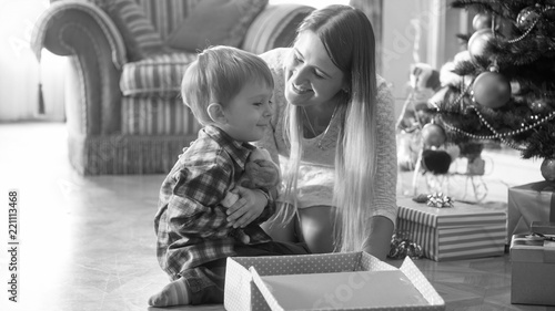 Black and white portrait of cheerful little boy hugging plush toy he received for CHristmas