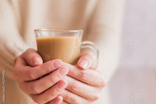woman in beige sweater holding a glass cup with coffee to get warm.