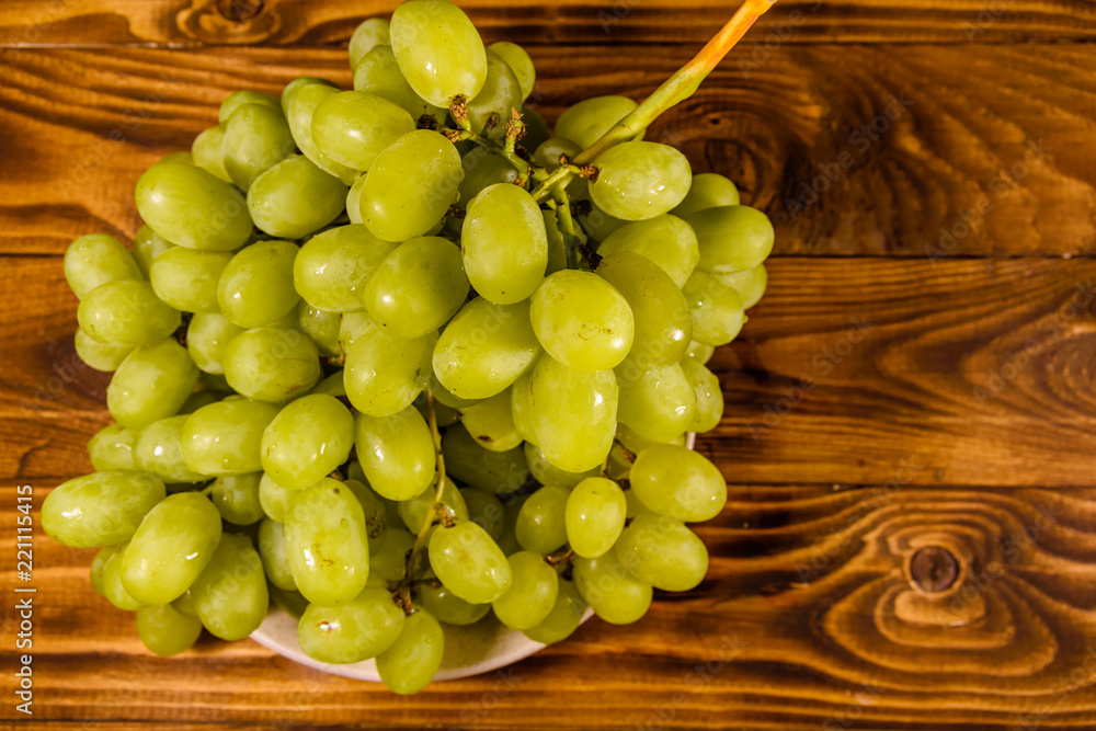 Ceramic plate with green grapes on wooden table. Top view Ceramic plate with green grapes on wooden table. Top view