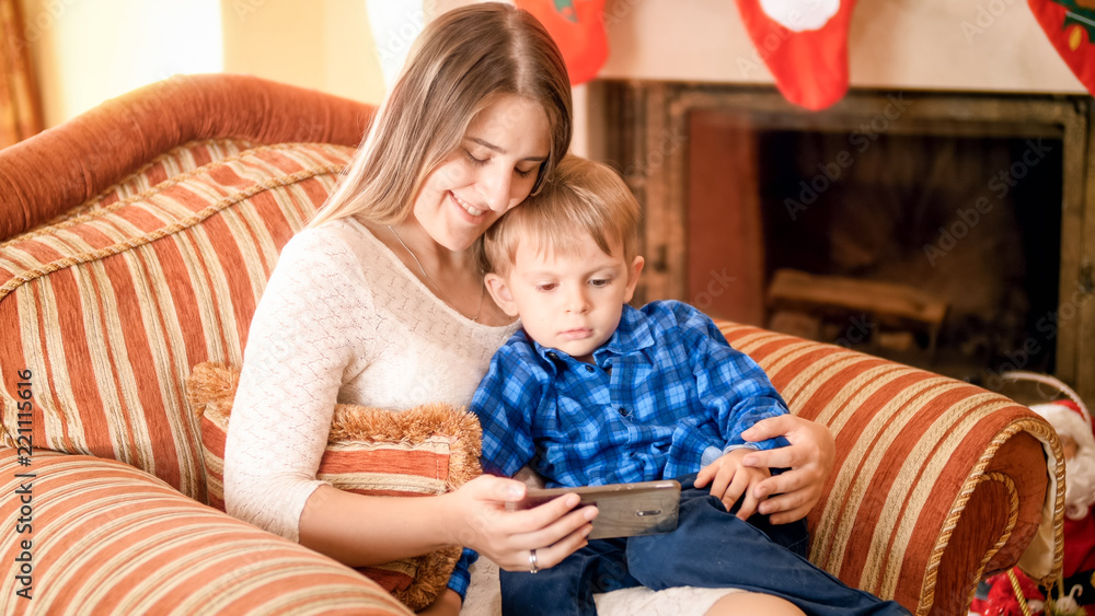 Portrait of beautiful smiling young woman resting in armchair with her little boy and watching cartoons Portrait of beautiful smiling young woman resting in armchair with her little boy and watching cartoons