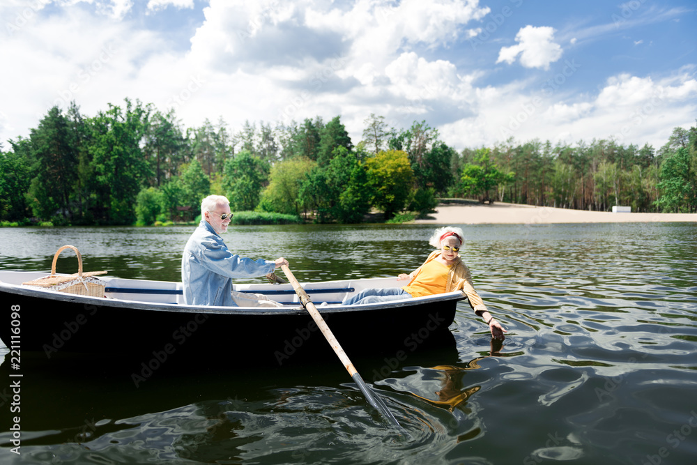 Hand in water. Elderly lady wearing yellow spotted shirt putting her hand in water while sitting in boat with her man