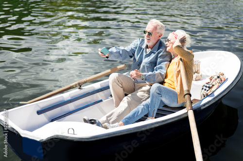 Posing for photo. Beaming elderly lady posing for photo with her bearded stylish husband while sitting in boat