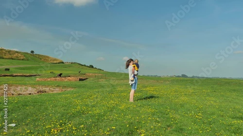 Young mom walking with her beautifull son on green field at mild sunny day