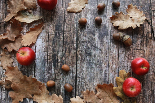 Dry fall leaves, red apples and acorns on wooden desk. September harvest, thanksgiving concept. Oak, planks, autumn background, copy space