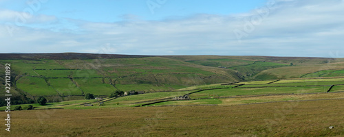 wide panoramic view of yorkshire dales landscape with fields and farmhouses enclosed by stone walls with open moorland above with blue sky and clouds