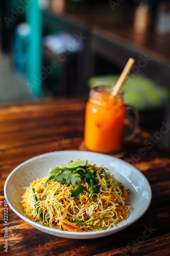 Healthy Vegetarian vegan menu Delicious Singapore style Stir fried rice noodles with carrot orange smoothies on wooden table in cafe