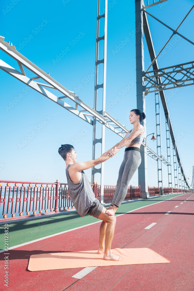 Inner power. Concentrated appealing woman and man training yoga pose and standing on bridge