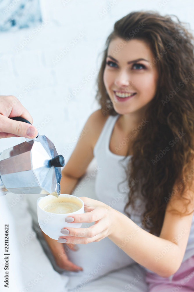 partial view of man pouring coffee to beautiful smiling woman in bedroom partial view of man pouring coffee to beautiful smiling woman in bedroom