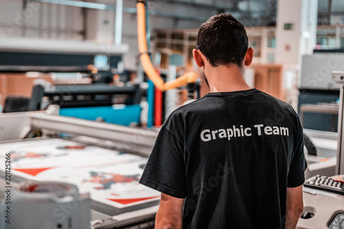 Young worker, operating a CNC machine. Big vinyl rolls ready for high quality printing. Industrial plotting service facility, International delivery system. Advertising and press business.