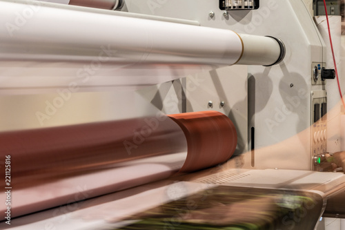 Big printing laminator armed with glossy paper rolls and transparent film.