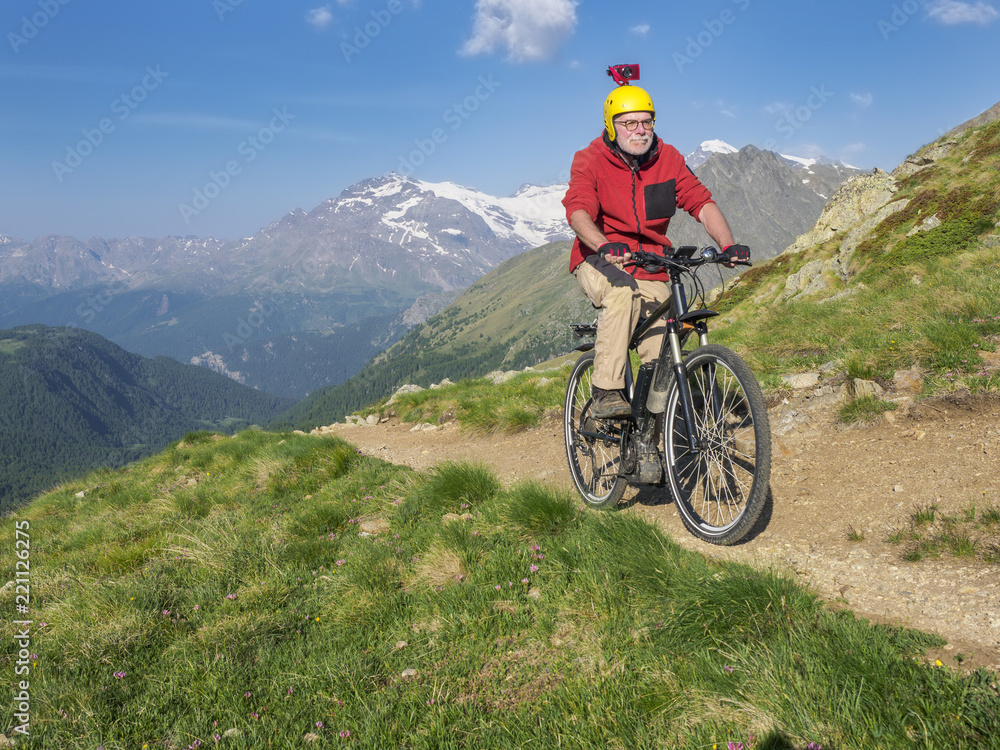Italy Lombardy, Passo di Val Viola, Man riding e-bike in the mountains with action cam on his helmet Italy Lombardy, Passo di Val Viola, Man riding e-bike in the mountains with action cam on his helmet