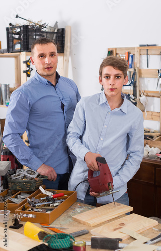 father and son with  fret saw cutting wood plank in  garage