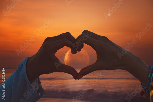 Silhouette of couple making heart - shape symbol with Moon rising from ocean   sea horizon.