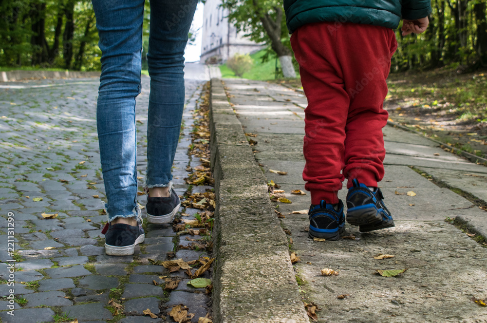 Mom and son are walking along the park avenue. View of the back of the lower body. Mom and son are walking along the park avenue. View of the back of the lower body.