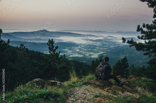 Hiker enjoying in the view on the valley and hills in the mist at sunrise