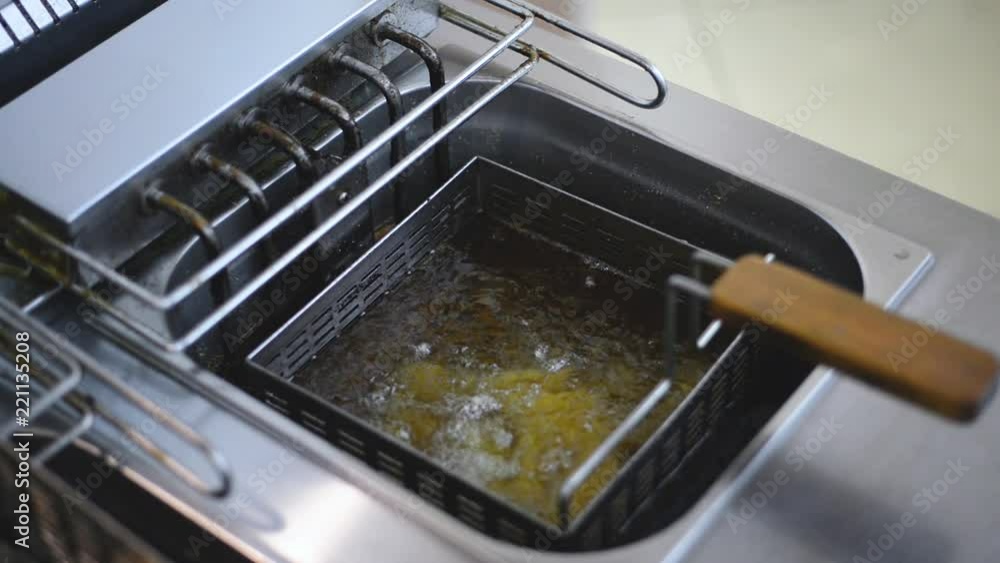 cook lowers into boiling oil fryer with wedges potato Metal box can for raw potato The kitchen of fast food restaurant cook lowers into boiling oil fryer with wedges potato Metal box can for raw potato The kitchen of fast food restaurant