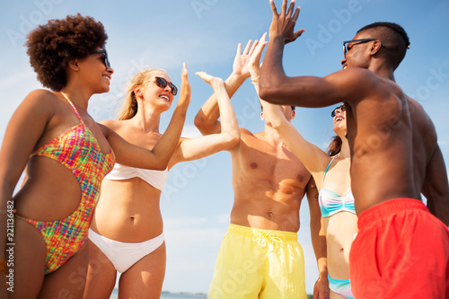 friendship, summer holidays and people concept - group of happy friends making high five on beach