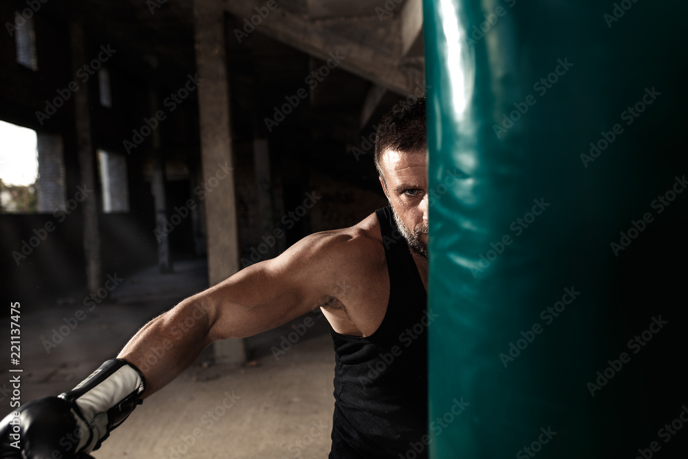 Male boxer punching a boxing bag in warehouse.