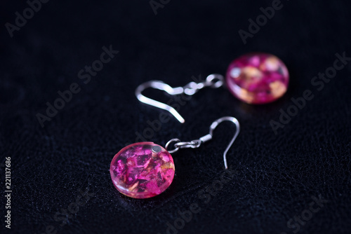 Resin earrings with dry rose petals on a dark background close up