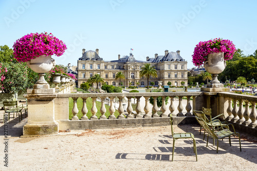 View of the Luxembourg palace in Paris, France, which houses the Senate since 1958, facing the Luxembourg garden, with typical metal lawn chairs, stone railing and vase with flowers in the foreground. photo