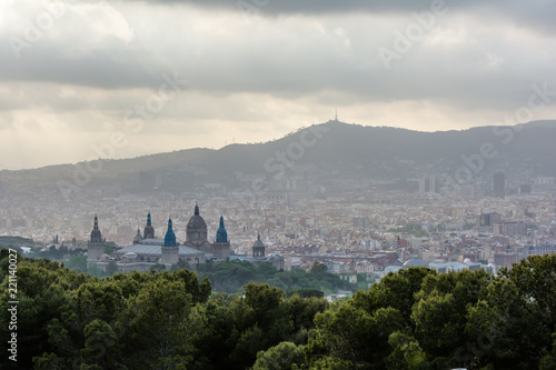 View to Barcelona city from the Montjuic hill in cloudy evening with The Palau Nacional (National Palace) Renaissance domes in the foreground. Barcelona evening skyline under cloudy sky.