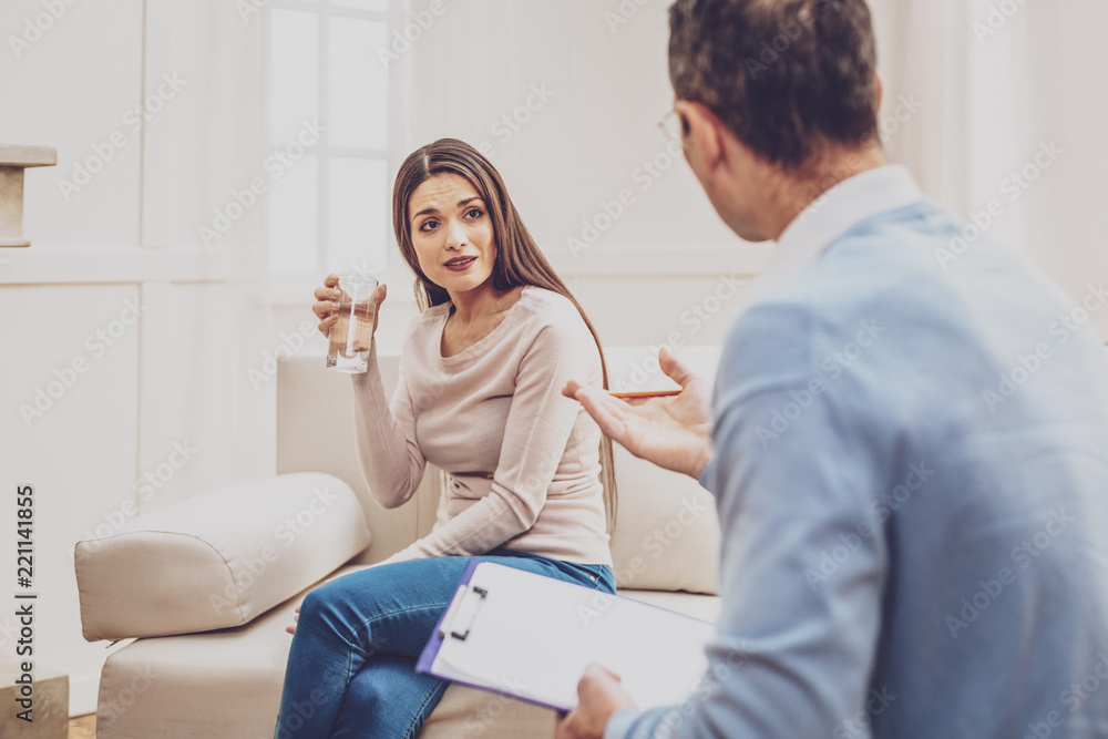 I am worried. Depressed young woman drinking water while listening to his doctors advice I am worried. Depressed young woman drinking water while listening to his doctors advice