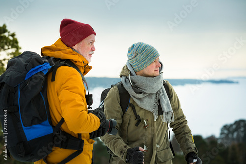 Wallpaper Mural Two mature men with exploring Finland in winter. Travellers hiking and Taking pictures with camera on the top of rock. Beautiful view of northern landscape with frozen Baltic Sea and snowy islands. Torontodigital.ca