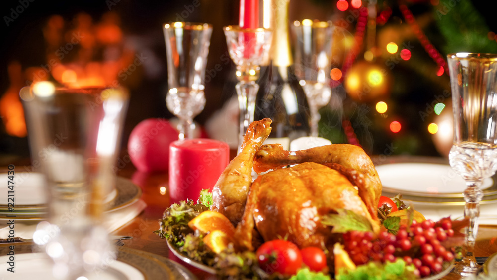 Closeup photo of hot baked chicken on festive table against Christmas tree and fireplace