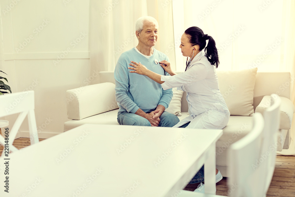 Preventive visit. Cheerful elderly man sitting on a sofa while a female doctor listening to his heart beating and lungs. Preventive visit. Cheerful elderly man sitting on a sofa while a female doctor listening to his heart beating and lungs.