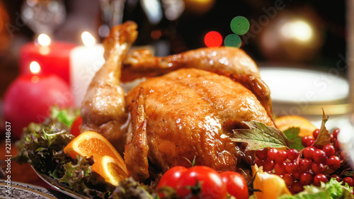 Closeup image of tasty baked chicken against glowing Christmas lights and burning candles photo