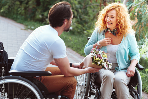 Completely amazed. Selective focus on a disabled lady beaming while getting surprised by her soulmate holding a beautiful bouquet.