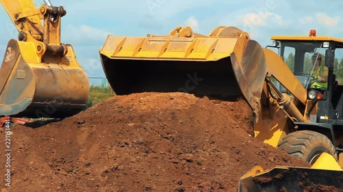 Wheel loader and excavator working on construction site. Heavy machinery in mining quarry. Wheel bulldozer moving soil in scoop. Close up of excavator bucket working on building territory