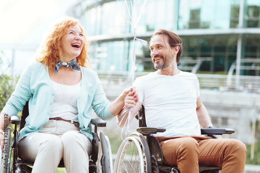 Having fun together. Extremely happy mature couple getting exited while driving their wheelchairs and holding balloons outdoors. Having fun together. Extremely happy mature couple getting exited while driving their wheelchairs and holding balloons outdoors.