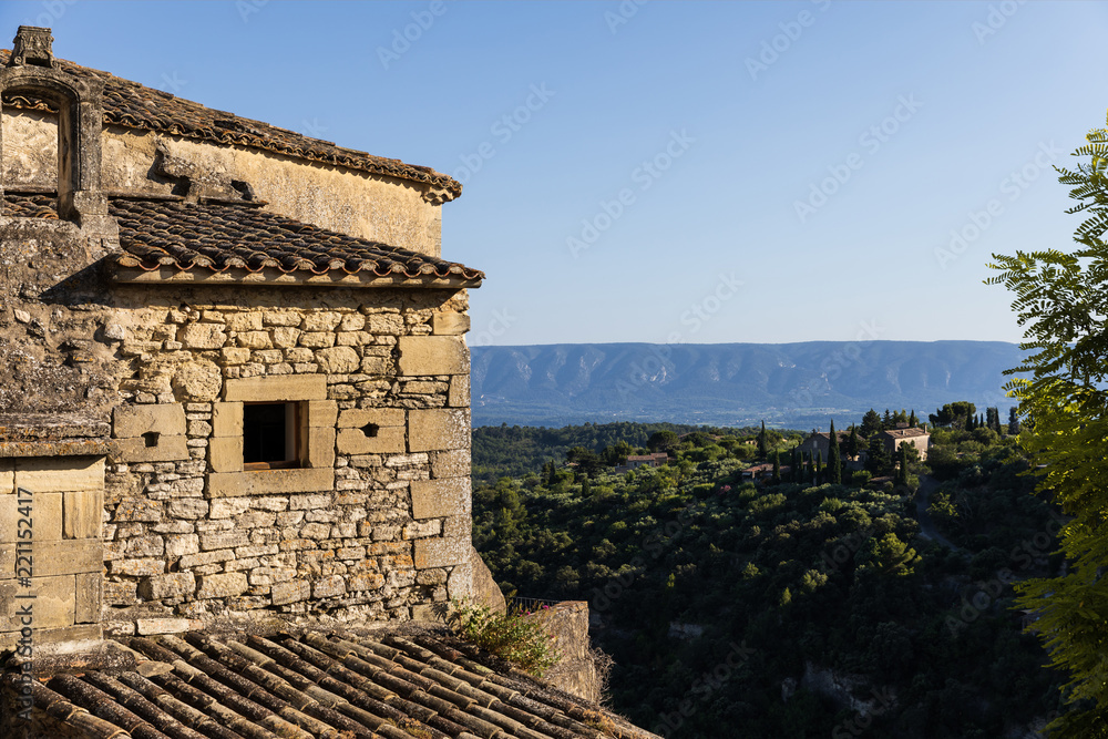 old stone building and roof, green vegetation and distant mountains in provence, france