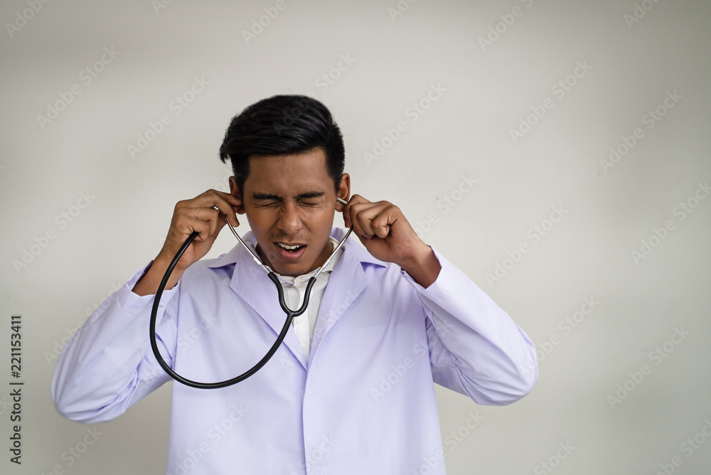The doctor is wearing white uniform, putting the stethoscope on his ears,unhappy face,stress and crazy feeling The doctor is wearing white uniform, putting the stethoscope on his ears,unhappy face,stress and crazy feeling