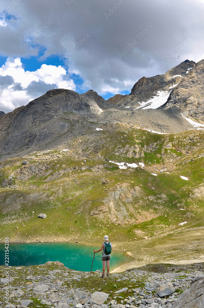 hiker standing near of a blue lake in hight alpine mountain