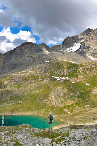 hiker standing near of a blue lake in hight alpine mountain