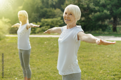 Feeling better. Waist up shot of a joyful senior lady grinning broadly and stretching out her arms while enjoying her group workout outdoors.