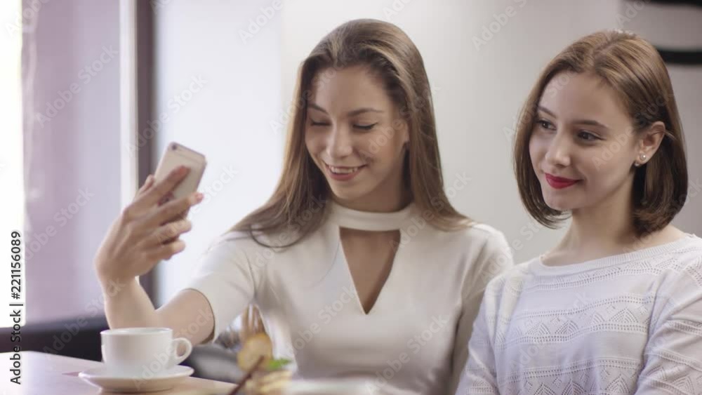 Two young women are sitting in a cafe and chatting. It is a friend meeting. Girls are sitting in the cafe at the table during coffee break. They are talking and drinking coffee. Thwy are making Two young women are sitting in a cafe and chatting. It is a friend meeting. Girls are sitting in the cafe at the table during coffee break. They are talking and drinking coffee. Thwy are making