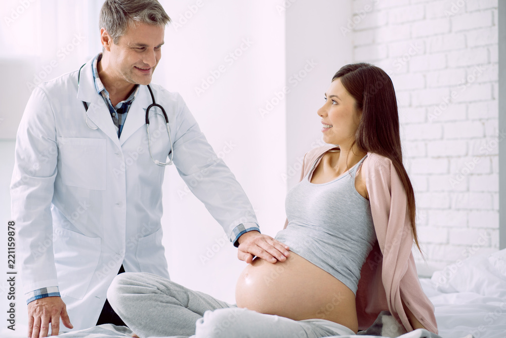Obraz premium Pregnant patient. Nice positive pleasant woman looking at her doctor and smiling while being in the hospital