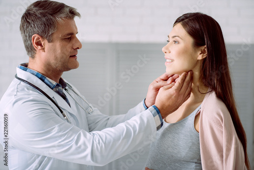Professional medical checkup. Nice professional male doctor standing opposite his patient and holding her neck while doing a checkup