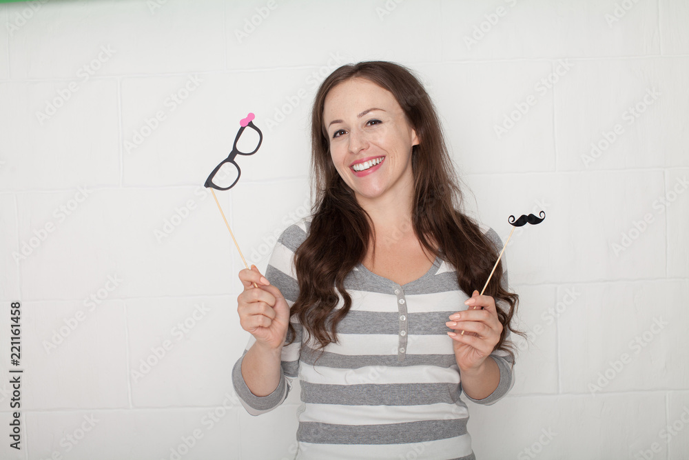 Young smiling woman wear white singlet and holding big glasses-mask, white wall on background Young smiling woman wear white singlet and holding big glasses-mask, white wall on background