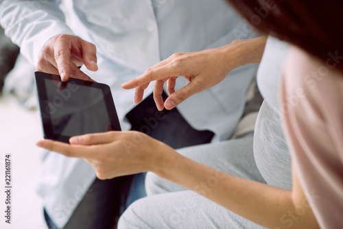 Digital device. Close up of a modern tablet being used by a positive nice pregnant woman while talking to her doctor