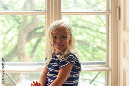 Portrait of little blonde girl sitting in sunny window