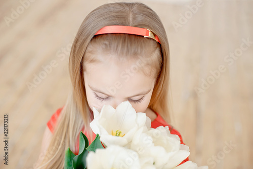 Close-up Portrait of a little girl child in red dress looking at a bouquet of white tulips indoor. photo