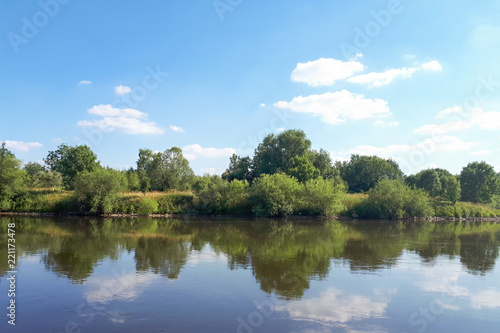 Fototapeta Naklejka Na Ścianę i Meble -  Clean water in the river. The water mirror reflects white clouds. A beautiful view on a sunny day.