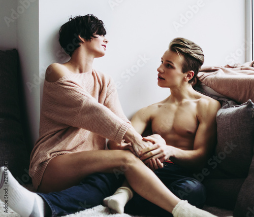 Beautiful happy couple sitting on the floor on a small mat in a large light room.