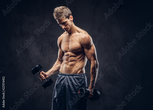 Handsome shirtless man with stylish hair and muscular ectomorph body doing the exercises with dumbbells.