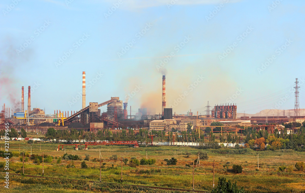 Panoramic view of the large industrial plant with smoking factory chimneys on blue sky background.
