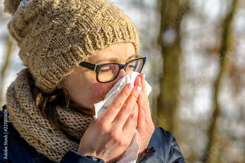 Woman with cold nose blowing in a tissue. Autumnal sick or people with cold and flu in autumn, outdoor.